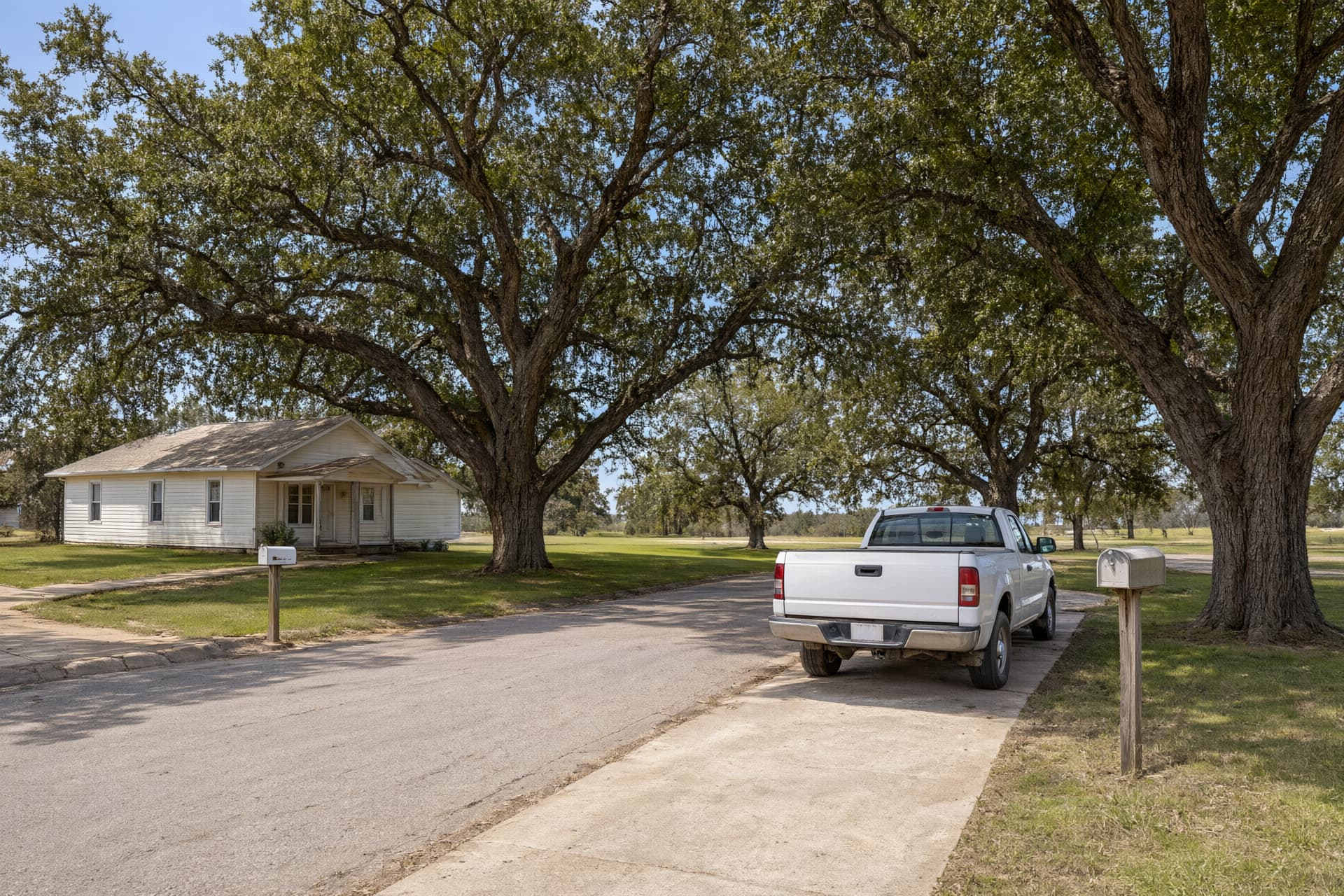 Small white house and big water oaks along a quiet street with a pickup in the driveway, typical of Bay, AR